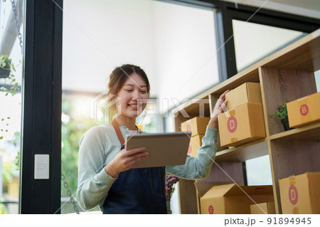 A portrait of a small startup, an SME owner, an Asian female entrepreneur checking orders to arrange the produce before packing the products in the inner boxes with the customers. Freelance concepts. 91894945