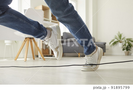Man or woman falls down after stumbling over an electrical cord on the floor at home Man or woman falls down after stumbling over an electrical cord on the floor at home 91895799