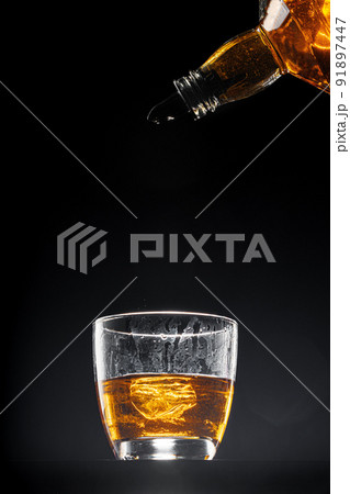 Whisky pouring into a glass on black background Whisky pouring into a glass on black background 91897447