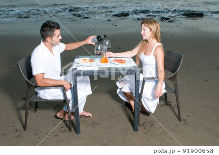 Young couple dressed in white celebrating a romantic dinner on the beach 91900658