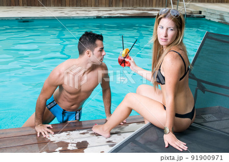 couple having a cocktail by the pool while enjoying the sun in spring or summer couple having a cocktail by the pool while enjoying the sun in spring or summer 91900971