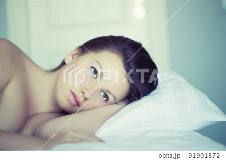 A young woman with huge frightened open eyes lying in bed and covers herself with the sheets and hides. Nightmares, insomnia, phobias, panic attacks. Concept A young woman with huge frightened open eyes lying in bed and covers herself with the sheets and hides. Nightmares, insomnia, phobias, panic attacks. Concept 91901372
