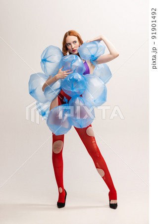 Portrait of beautiful girl with bright makeup in red torn tights posing with plastic bags with water isolated over grey background 91901492