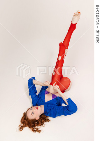 Portrait of beautiful young girl in blue shirt and red tights lying on floor, posing isolated over grey studio background 91901548