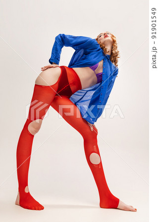 Portrait of stylish young girl in blue shirt and red torn tights posing isolated over grey studio background 91901549