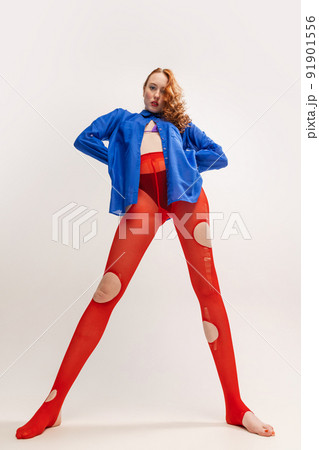 Portrait of beautiful young girl in blue shirt and red torn tights posing isolated over grey studio background. Extraordinary, weird look 91901556