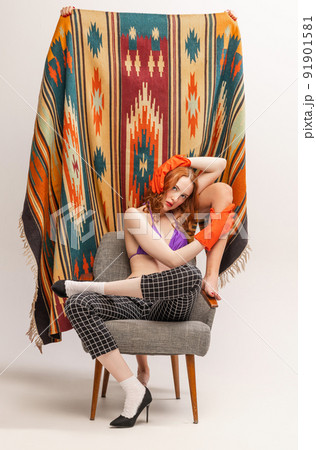 Portrait of beautiful red-haired girl posing in swimming suit top and rubber gloves near colorful carpet isolated on grey background Portrait of beautiful red-haired girl posing in swimming suit top and rubber gloves near colorful carpet isolated on grey background 91901581