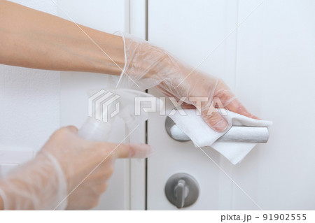 Cleaning door handles with wet wipe and white gloves. Sanitize surfaces prevention in hospital and public spaces against corona virus. Woman hand using towel for cleaning home room door link. 91902555