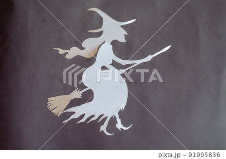 White paper witch on a broom. Halloween attribute cut out of a sheet of paper with scissors. Flying in the air silhouette of a witch in a pointed hat White paper witch on a broom. Halloween attribute cut out of a sheet of paper with scissors. Flying in the air silhouette of a witch in a pointed hat 91905836