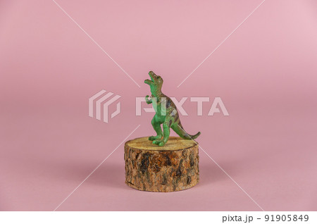 Miniature dinosaur on a pedestal against a pink background. A small figurine of a predatory dinosaur on a round pine stand. Selective Focus. Miniature dinosaur on a pedestal against a pink background. A small figurine of a predatory dinosaur on a round pine stand. Selective Focus. 91905849