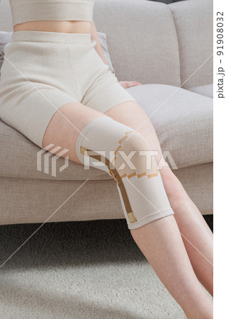 Knee support brace on a woman leg. girl in an orthosis in the interior of the house. Orthopedic anatomic braces for knee fixation, injuries and pain. Knee Joint Bandage Sleeve. Elastic Sports. 91908032