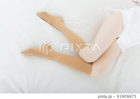 Beige compression stockings on a woman in a white room. Knee socks or socks. Girl putting on stockings at home. Beautiful female legs. 91909875