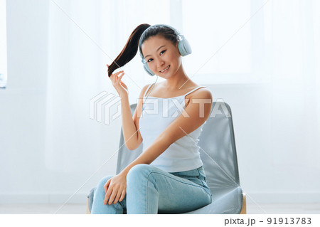 Smiling cheerful tanned lovely young Asian woman in headphones touches hair looks at camera at home interior living room. Sound Studio Stream, Social media concept. Cool offer Banner Wide angle Smiling cheerful tanned lovely young Asian woman in headphones touches hair looks at camera at home interior living room. Sound Studio Stream, Social media concept. Cool offer Banner Wide angle 91913783