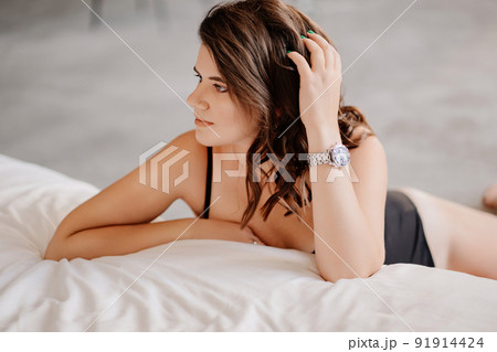an attractive brunette woman in a black bodysuit by the bed in the bedroom. an attractive brunette woman in a black bodysuit by the bed in the bedroom. 91914424