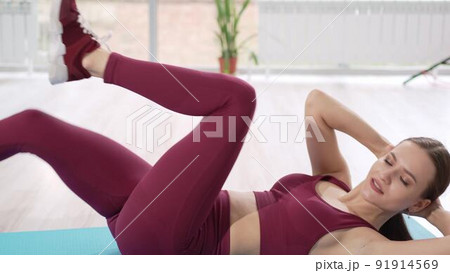 a beautiful and athletic girl in a burgundy tracksuit does exercises for the abs 91914569