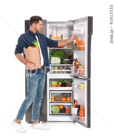 Man with bag of groceries near open refrigerator on white background Man with bag of groceries near open refrigerator on white background 91915533