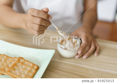 Home lifestyle concept, Hands of woman scooping yogurt and eating crackers for snack at home 91925013
