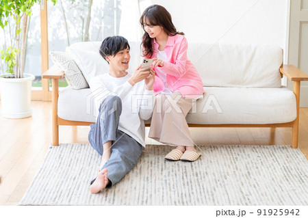 リビングでスマホを操作するカップル リビングでスマホを操作するカップル 91925942