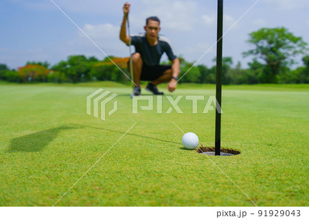 Golfer putt golf ball into hole on the green at golf course Golfer putt golf ball into hole on the green at golf course 91929043