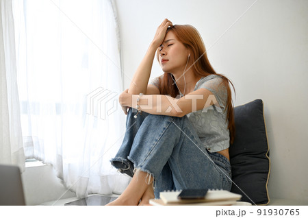 Frustrated young Asian woman sitting in her home living room, thinking her life problems 91930765