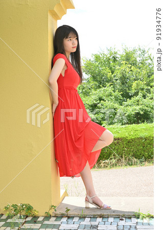 黄色い壁に佇む赤いワンピースの女性 91934776