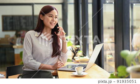 Successful young asian woman investor having phone conversation and using laptop at coffee shop 91935051