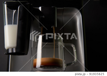 Freshly brewed coffee is poured from the coffee machine into glass cups. 91935625