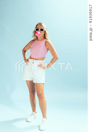 Portrait of stylish young woman in trendy sunglasses posing with bubble gum isolated over light blue studio background 91936917