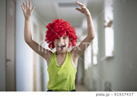 A child in a bright wig. Funny boy with red artificial hair. Artist schoolboy A child in a bright wig. Funny boy with red artificial hair. Artist schoolboy 91937437