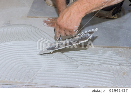 Putting adhesive on the bathroom floor by spreading wet mortar before applying tiles Putting adhesive on the bathroom floor by spreading wet mortar before applying tiles 91941437