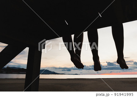 Silhouette feet of couple sitting on the pier at sunset beach. 91941995