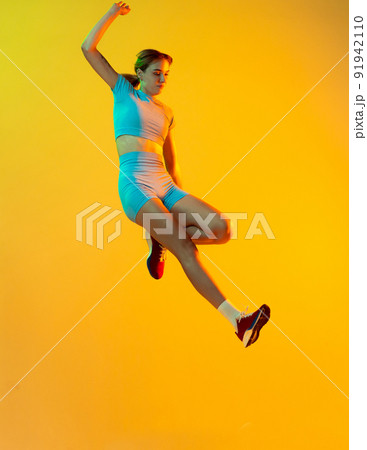 Professional longjumper. One female athlete in sports uniform jumping isolated on yellow background. Concept of sport, action, motion, speed. Professional longjumper. One female athlete in sports uniform jumping isolated on yellow background. Concept of sport, action, motion, speed. 91942110
