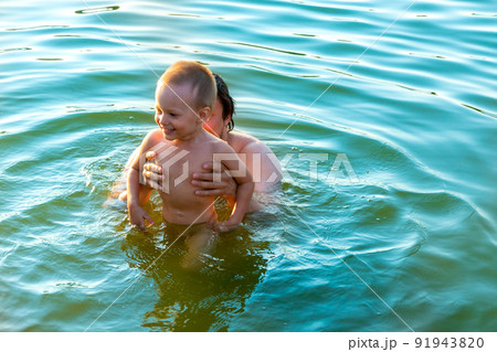 The little boy in his father's arms, in the waves of the sea. Dad with the little child on vacation. 91943820