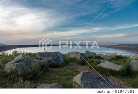 Upper water reservoir of the pumped storage hydro power plant Dlouhe Strane in Jeseniky Mountains, Czech Republic. During summer evening, sunset with blue sky and clouds. 91947981