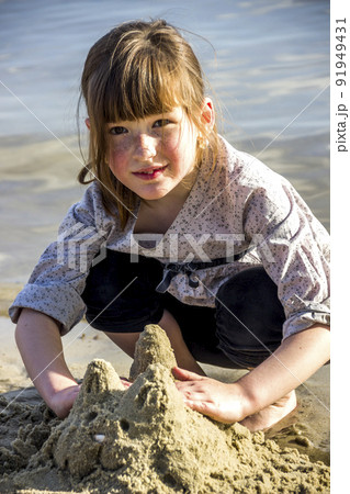 a little girl makes a sand sculture of cat 91949431