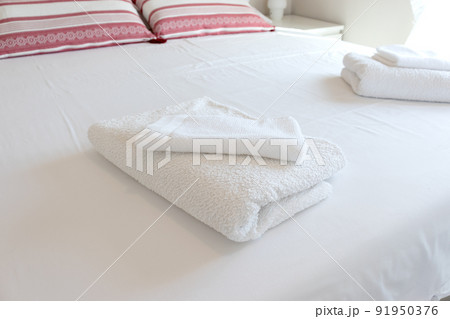 White folded towels on a hotel bed with white sheets. 91950376