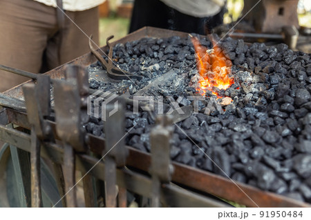 Close-up detail old medieval blacksmith furnace with hot burning coal flame forge iron metal. Craft smith farrier workshop fireplace with many professional craftsman tools equipment 91950484