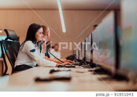 Female security guard operator talking on the phone while working at workstation with multiple displays Security guards working on multiple monitors Female security guard operator talking on the phone while working at workstation with multiple displays Security guards working on multiple monitors 91951043