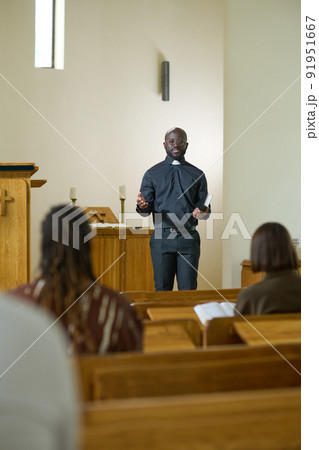 Young black man in shirt with clerical collar and pants preaching in church 91951667