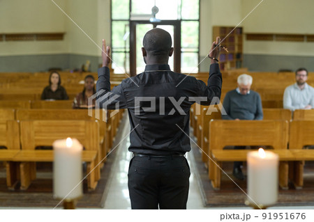 Back of African American priest in black shirt and pants blessing parishioners 91951676