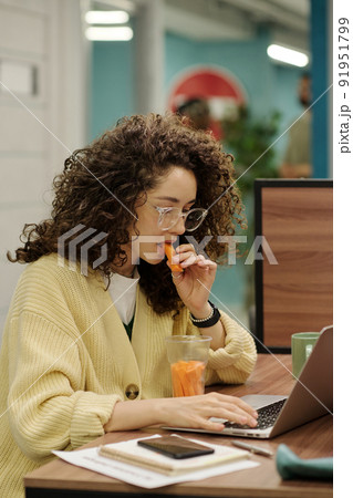 Young businesswoman eating fresh carrots while working in front of laptop 91951799