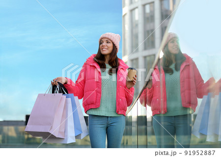 Beautiful young woman with cup of coffee and shopping bags near building Beautiful young woman with cup of coffee and shopping bags near building 91952887