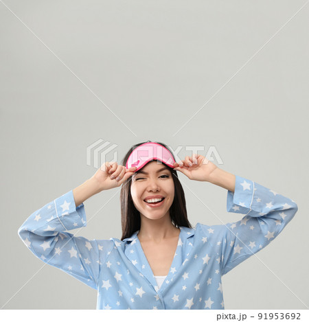 Beautiful Asian woman wearing pajamas and sleeping mask on light grey background. Bedtime Beautiful Asian woman wearing pajamas and sleeping mask on light grey background. Bedtime 91953692