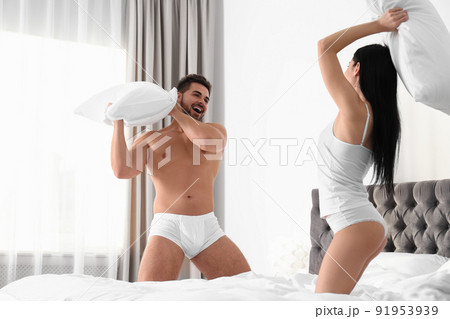 Young couple in white underwear having pillow - Stock Photo