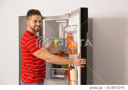 Young man taking fresh apple out of refrigerator Young man taking fresh apple out of refrigerator 91954245