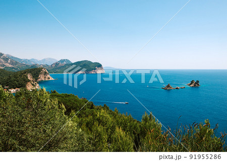 Picturesque view on rocks on a sunny day from the sea. Budva riviera, Montenegro. Aerial view of Sveti Nikola, Budva island, Montenegro. Hawaii beach, umbrellas and bathers and crystal clear waters 91955286