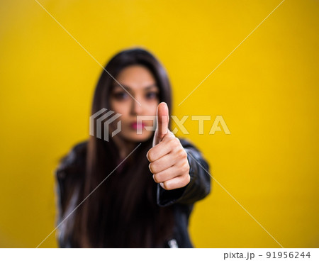 Young woman does a thumbs-up gesture - studio shot against yellow background 91956244