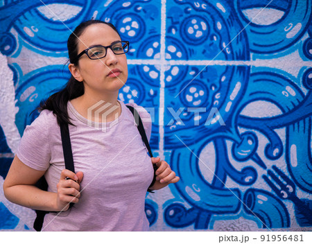 Young and beautiful woman leans against a colorful wall and poses for the camera - typical street 91956481