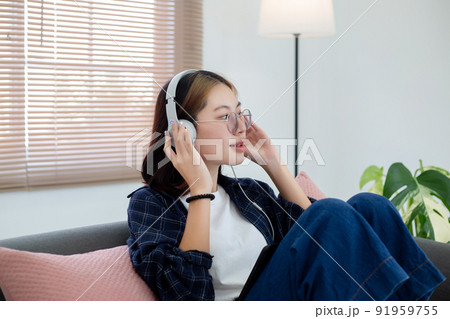 Happy Asian glasses girl listening music from headphone in living room at home. Recreation at home concept. Happy Asian glasses girl listening music from headphone in living room at home. Recreation at home concept. 91959755