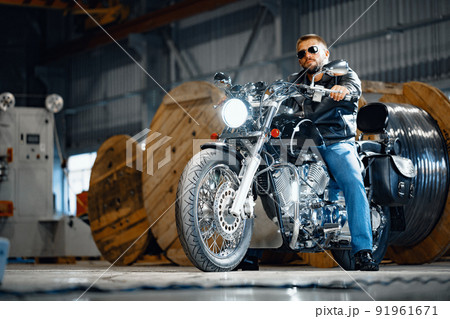 Bearded motorcyclist in black leather clothing with his motorbike Bearded motorcyclist in black leather clothing with his motorbike 91961671